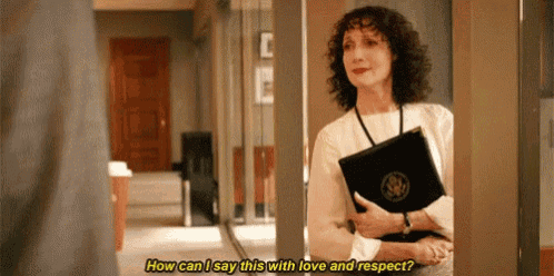 a woman is talking to a man in a hallway while holding a folder .