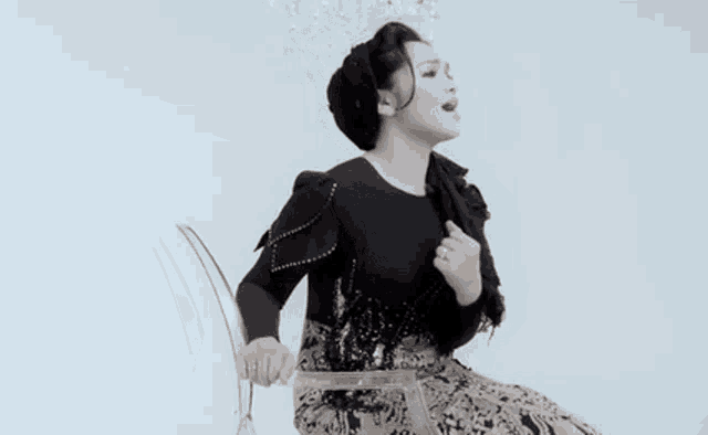 a woman in a black dress is sitting on a clear chair and singing .