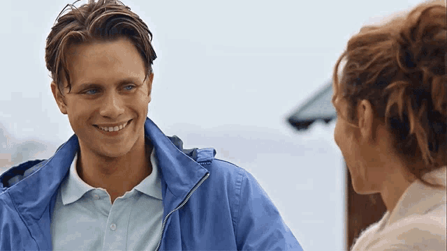 a man in a blue jacket smiles while looking at a woman