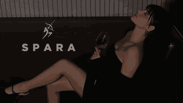 a woman in a black dress sits on a couch holding a glass of wine