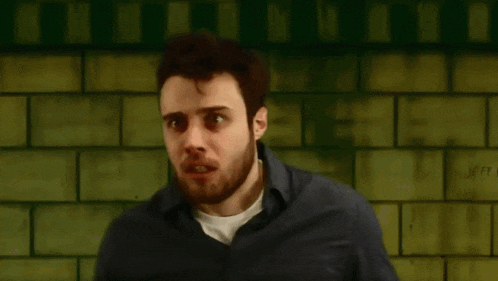 a man is biting his nails in front of a green brick wall