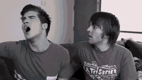 two men are sitting on a couch and one has a shirt that says a triseries
