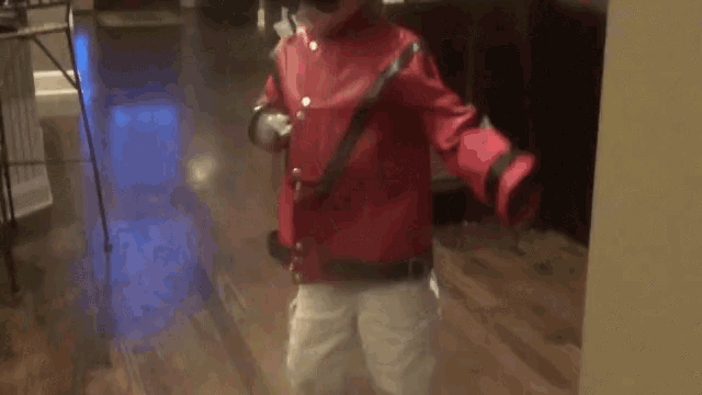 a young boy in a red jacket and white pants is walking down a hallway .