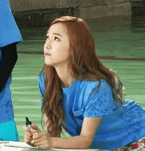 a woman in a blue shirt is sitting at a table with a pen in her hand