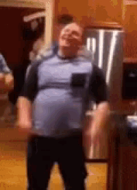 a man is dancing in a kitchen with a refrigerator in the background .