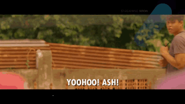 a man stands in front of a fence with the words yoohoo ash written on the screen