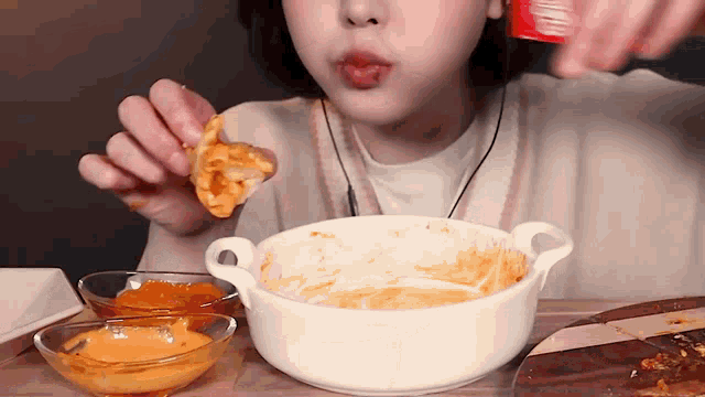 a woman is sitting at a table eating a bowl of food with sauces on it .