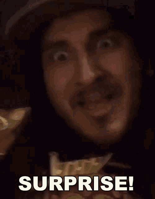 a man with long hair and a hat is holding a snickers bar and saying surprise .