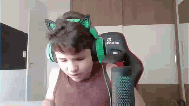 a young boy wearing headphones and a cat ear headband is standing in front of a microphone .