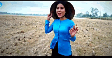 a woman wearing a blue shirt and a black hat is standing in a field .