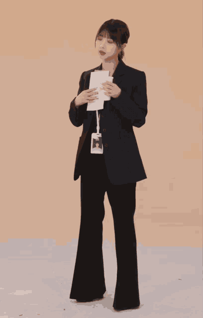 a woman in a black suit is holding a cup and a piece of paper