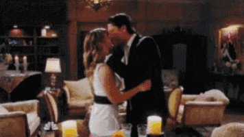 a man and a woman are kissing in a living room with candles on the table .
