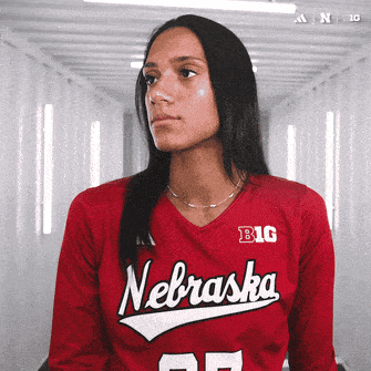 a woman wearing a red nebraska jersey looks to the side