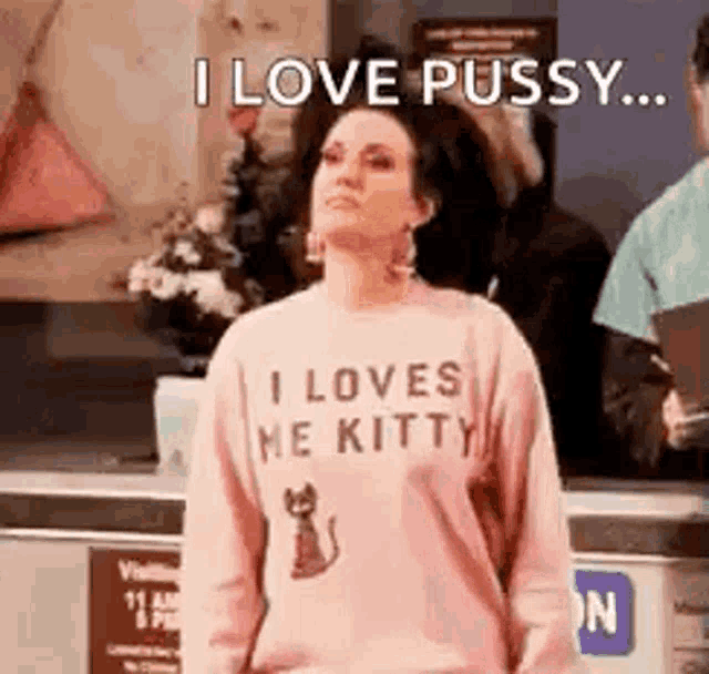 a woman wearing a pink sweater that says `` i love pussy ... '' is standing in a room .