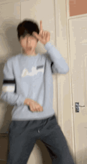 a young man in a light blue sweater is dancing in front of a white door