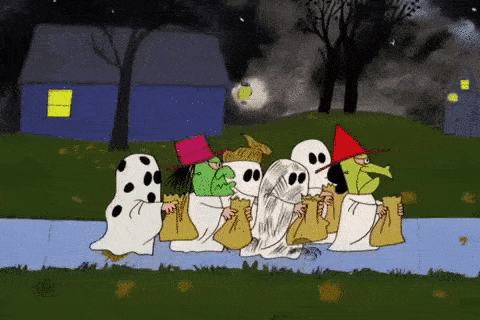 a group of peanuts characters dressed as ghosts are walking down the sidewalk .