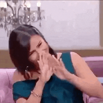 a woman is covering her face with her hands while sitting on a couch .