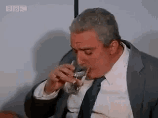 a man in a suit and tie is drinking from a glass while sitting down .
