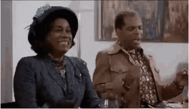 a man and a woman are sitting at a table . the woman is wearing a hat .