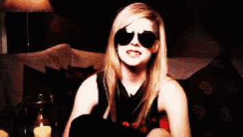 a woman wearing sunglasses is smiling in a dark room