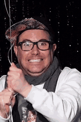 a man wearing glasses and a hat is smiling while holding a string