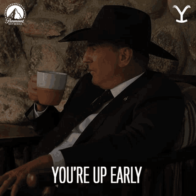 a man in a suit and cowboy hat says you 're up early while holding a cup of coffee