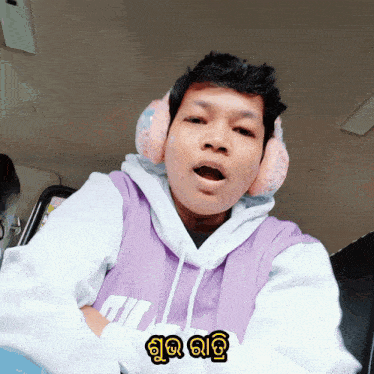 a man wearing pink ear warmers and a purple hoodie with a foreign language sticker