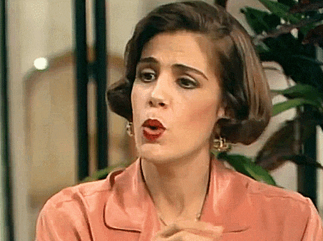 a woman in a pink shirt and earrings is making a funny face .