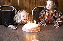 two little girls sitting at a table with a birthday cake