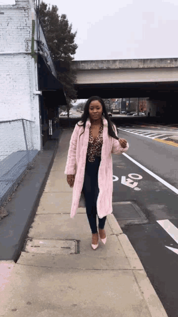 a woman in a pink coat is walking down a sidewalk near a bike lane