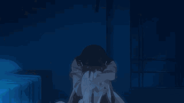 a person sitting in a dark room with their head in their hands