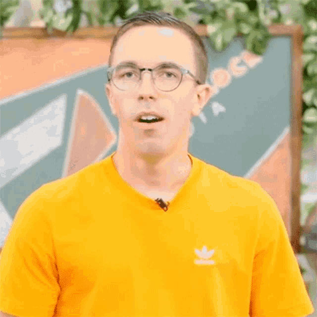 a man wearing glasses and a yellow adidas shirt smiles for the camera