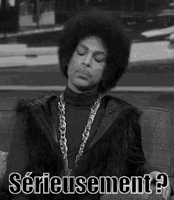 prince is sitting on a couch wearing a fur coat and a chain necklace .