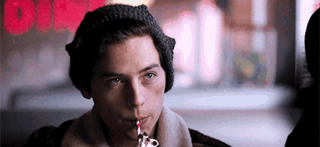 a young man is drinking through a straw while wearing a hat .