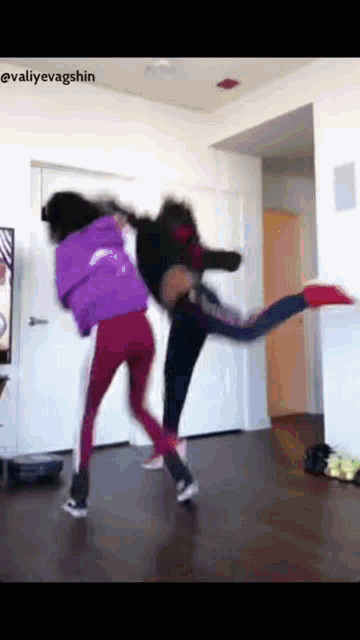 two girls are dancing in a living room and one of them is kicking the other in the air .