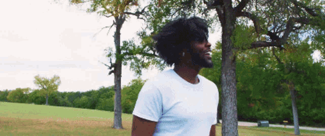 a man in a white shirt is standing in front of trees in a park
