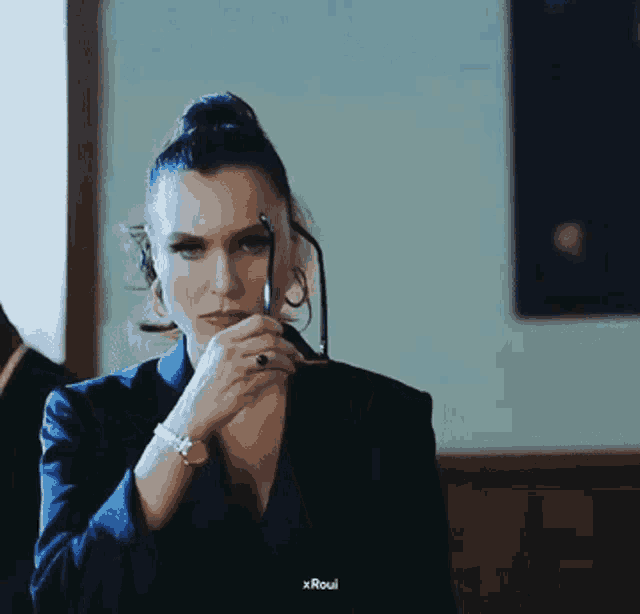 a woman in a suit is adjusting her glasses while wearing a watch