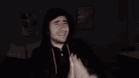 a man in a hoodie is clapping his hands in the dark in a room .
