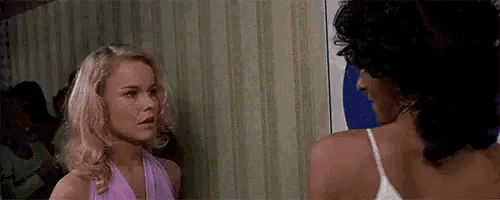 two women are standing next to each other in front of a striped wall and talking to each other .