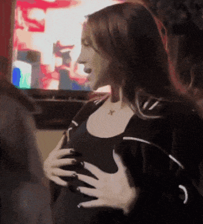 a woman in a black top is holding her chest while standing in front of a television .