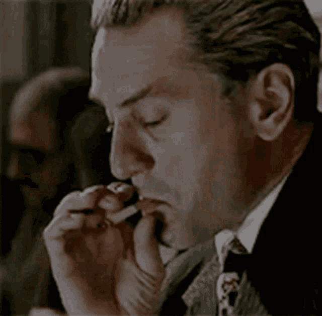 a man in a suit and tie is smoking a cigarette with his eyes closed