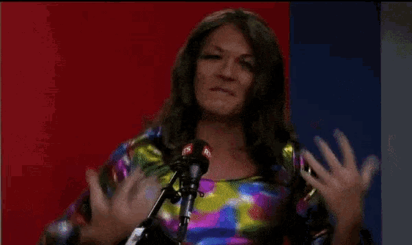 a woman in a colorful dress stands in front of a microphone with her hands in the air .