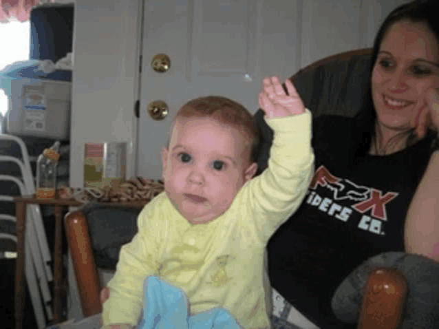 a baby sitting next to a woman wearing a shirt that says fox riders co.