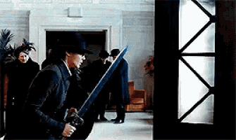 a man in a top hat is holding a sword in a hallway .