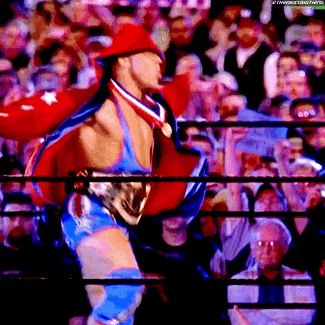 a wrestler in a red white and blue outfit with a medal around his neck stands in front of a crowd ..