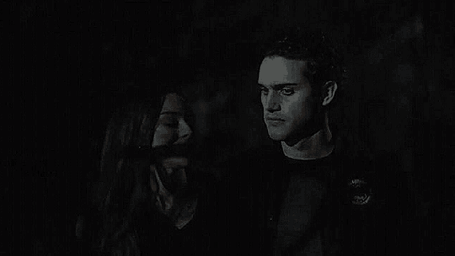 a man and a woman are standing next to each other in the dark looking at each other .