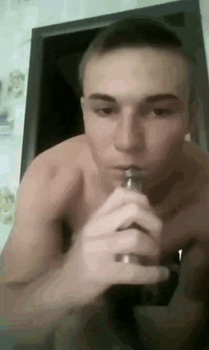 a shirtless man is smoking an electronic cigarette in front of a mirror .