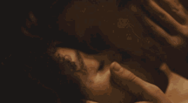 a close up of a woman laying down with her eyes closed and her hands on her head .