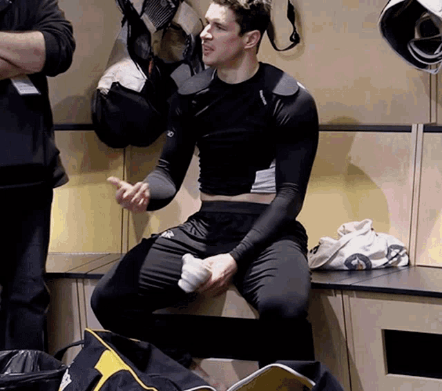 a man sits on a bench in a locker room with a bag that says ' reebok ' on it