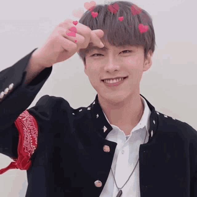 a young man wearing a black jacket and a red bandana making a heart with his fingers